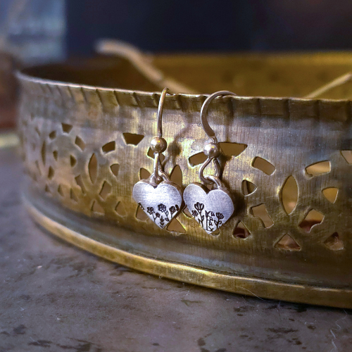 Heart Wildflower Dangle Earrings in Sterling Silver hanging from the edge of a bronze tray