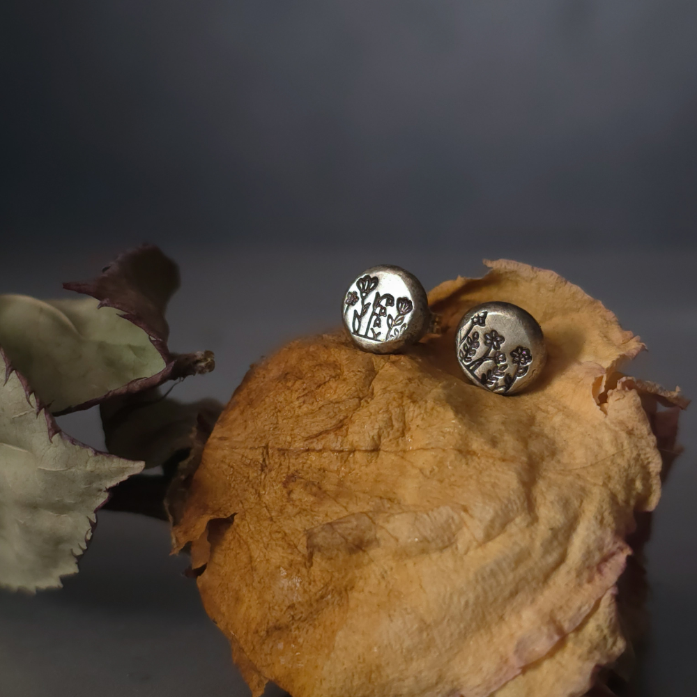 Silver earrings on a dried flower with a dark background