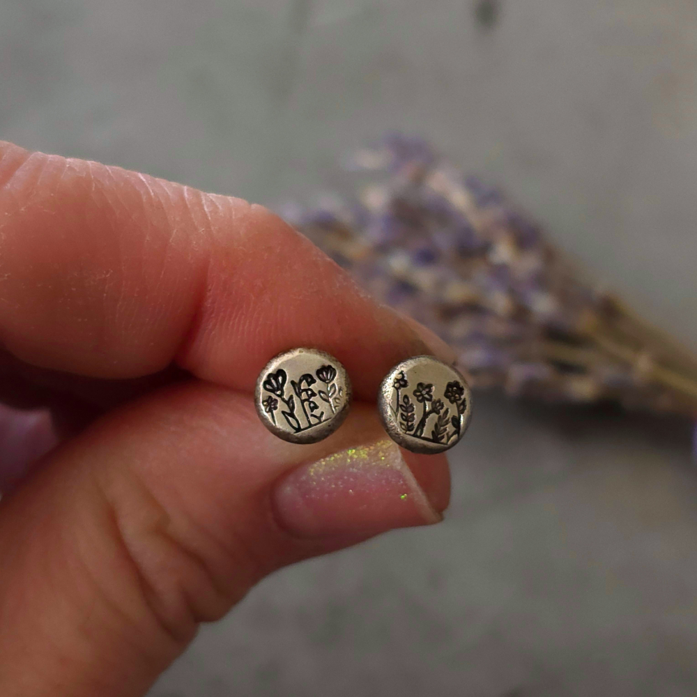 Silver earrings with floral design held between fingers against a blurred background