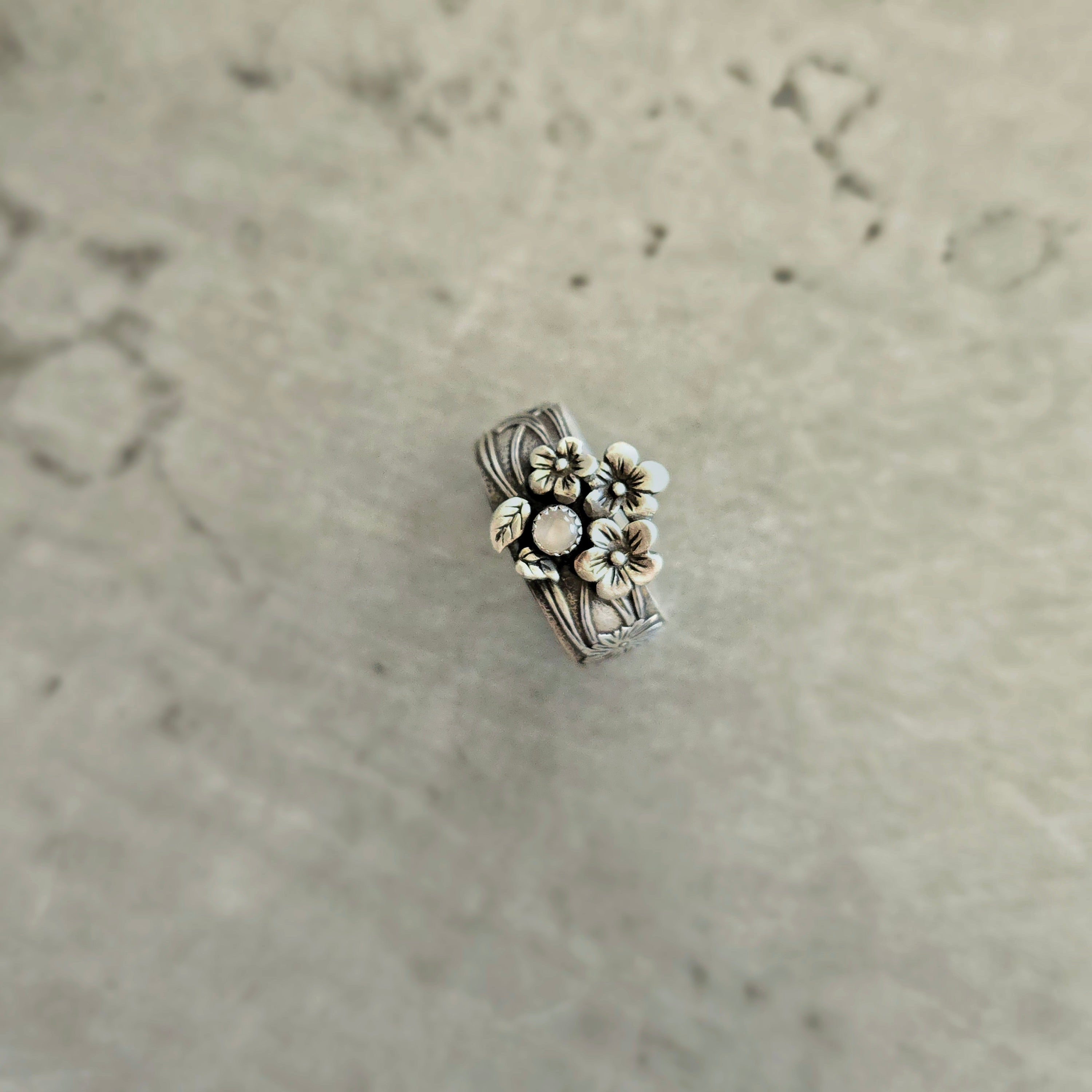 Top view of sterling silver floral band ring featuring moonstone and floral details