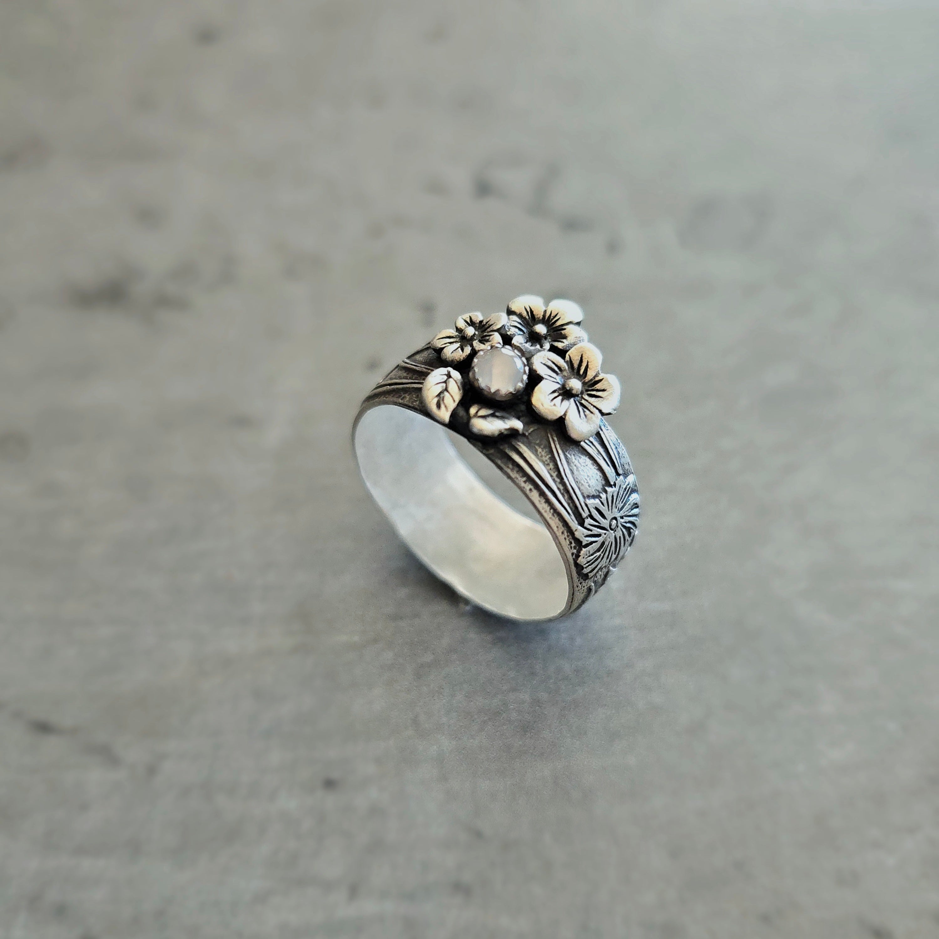 Sterling silver floral band ring with moonstone on neutral background