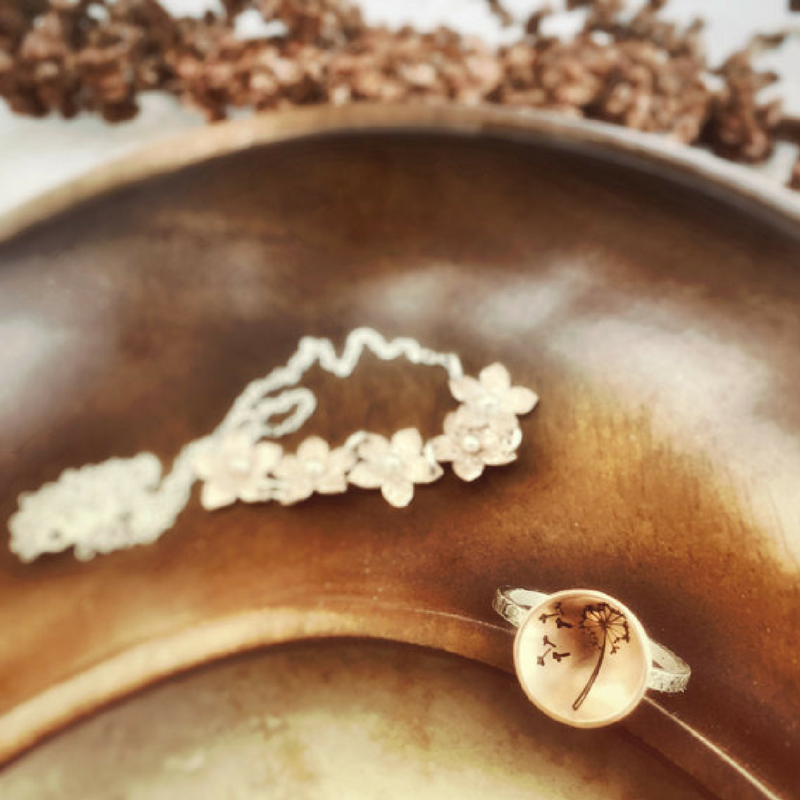 Dandelion Wish Ring with Copper and Silver in a jewelry dish photographed from top with another floral necklace design 