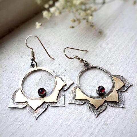 Lotus Hoop Earrings with Garnet photographed laid flat next to the window, there is some flowers at the background