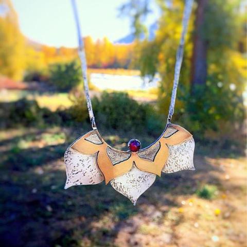 Lotus Statement Necklace with Garnet sterling silver and brass front view photographed outside with a lake and trees scenery at the background