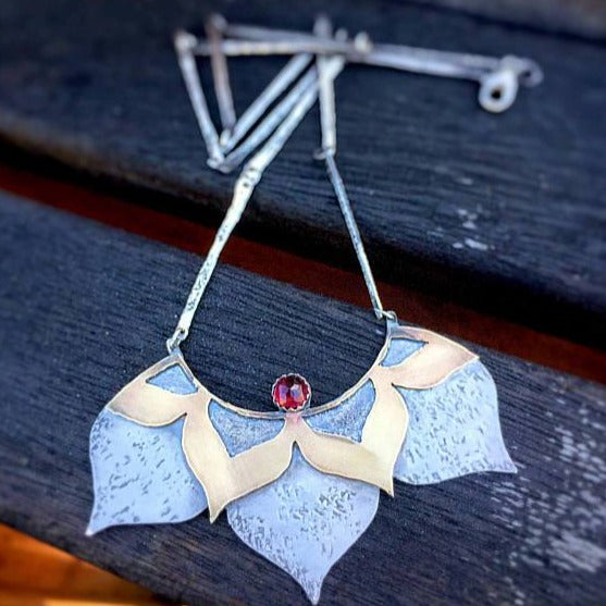 Lotus Statement Necklace with Garnet sterling silver and brass photographed on a wood table with blueish color ambiance
