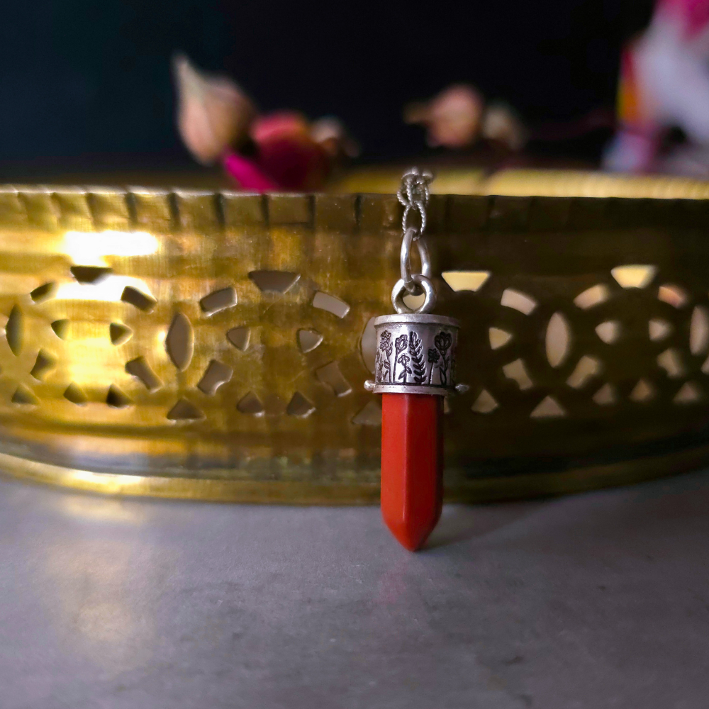 Red Jasper Charm pendant with silver top on a reflective surface with a blurred background