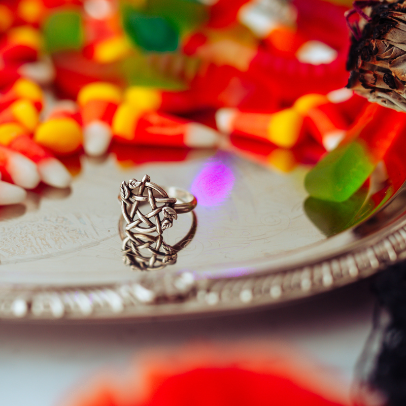 Sterling Silver Pentacle Ring with Leaves sitting on a metallic surface with colorful candy in the background