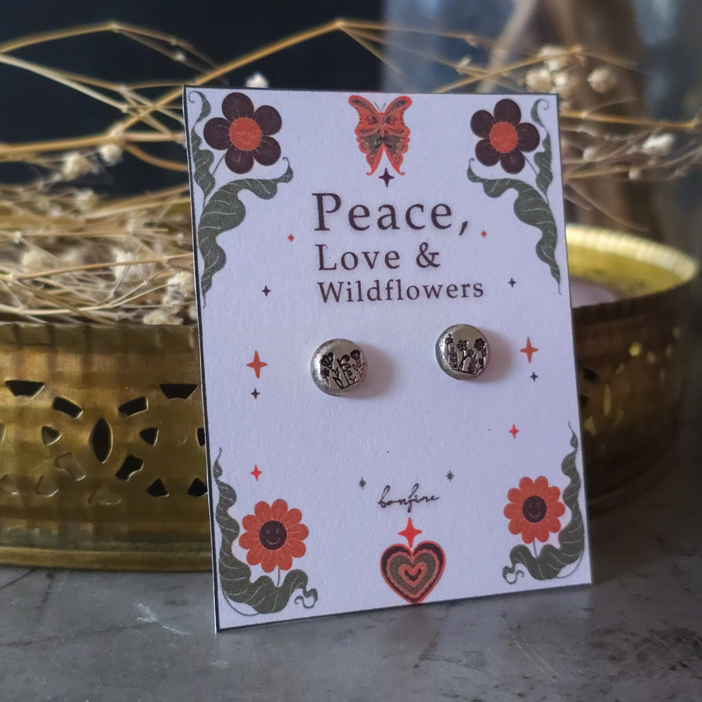 Pair of silver earrings on a 'Peace, Love & Wildflowers' themed card with decorative elements.