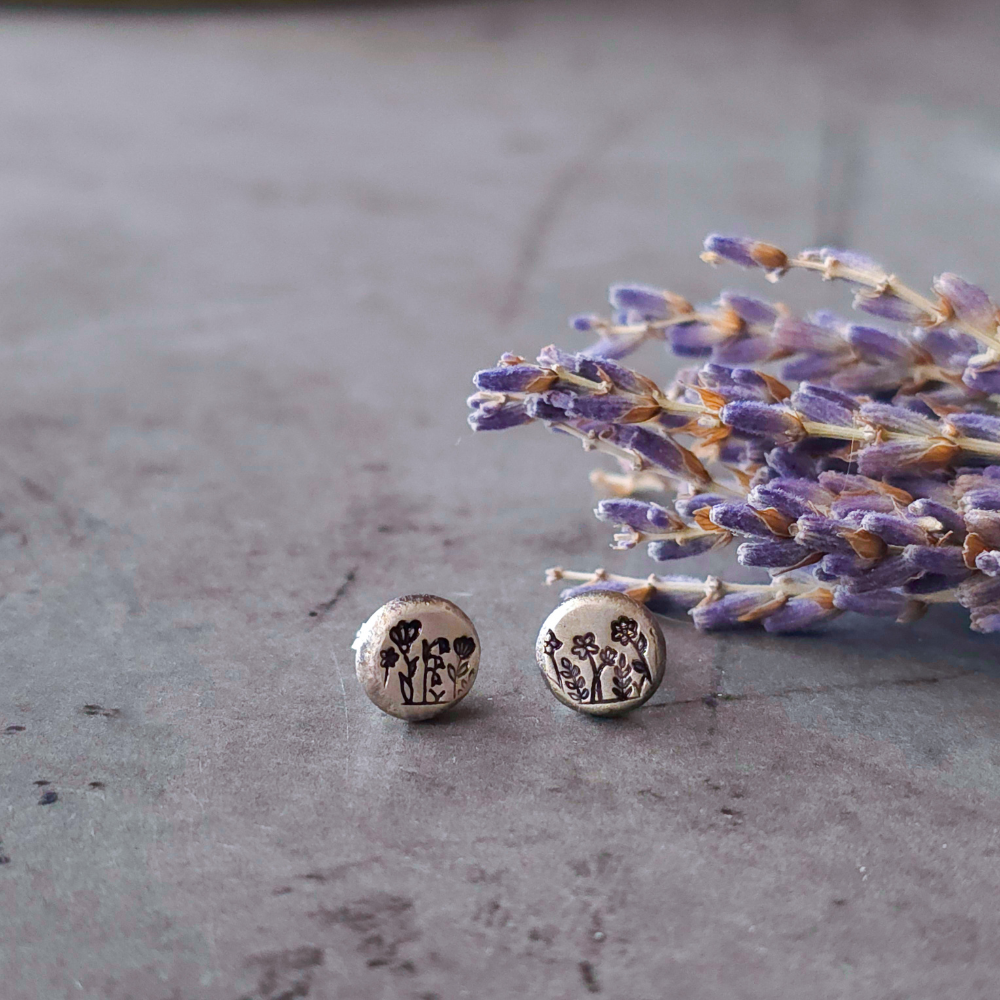 Silver stud earrings with floral design on a gray surface with lavender flowers.