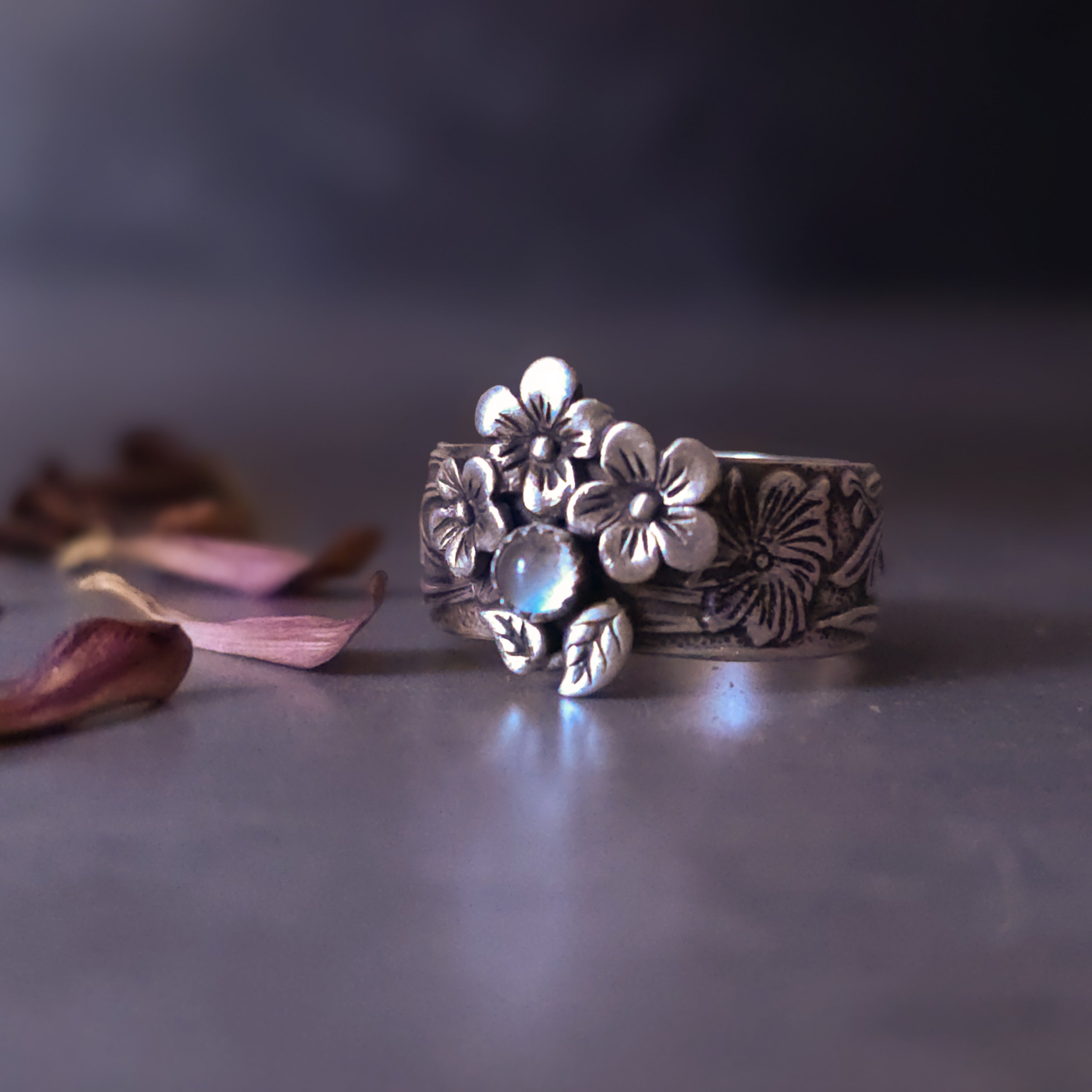 Sterling silver floral ring with moonstone on a dark surface with dried leaves
