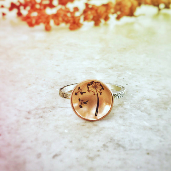 Dandelion Wish Ring with Copper and Silver front view laid on a marble and there is orange color flowers at the back ground that matches the ring 