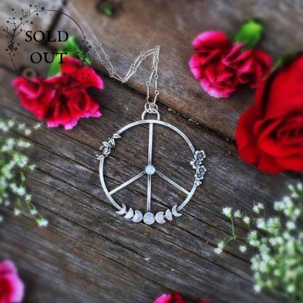 Moon Phases Peace Necklace with Moonstone laid flat on a wooden background surrounded with red roses and flowers