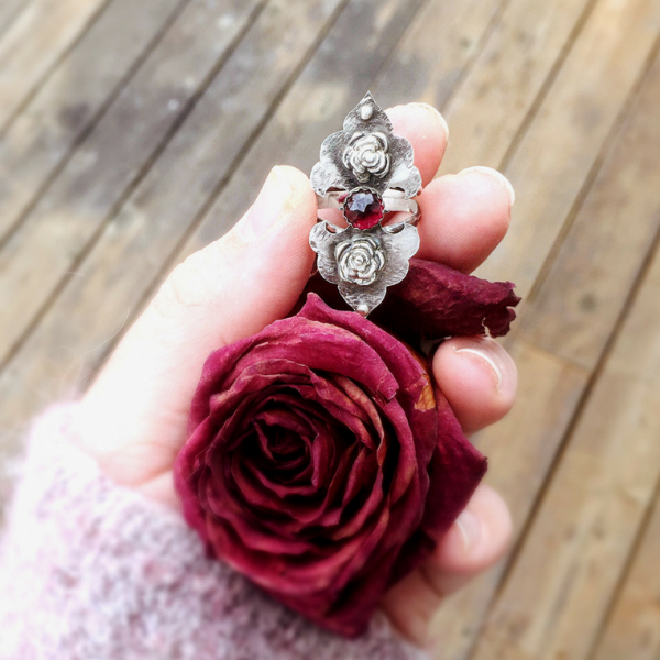 Rosebuds Flower Statement Ring with Garnet front view held in hand with a dried red rose