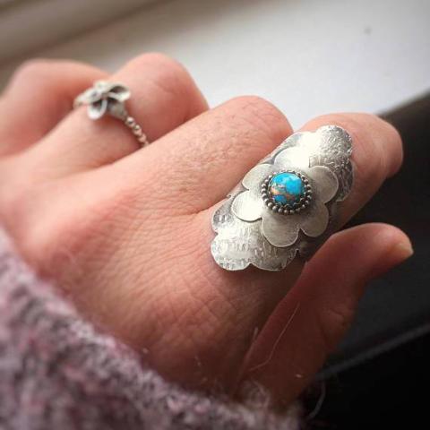 Turquoise Flower Statement Ring photographed on a finger, in which The stone is set on a simple flower design and centered in a circle of silver beads 